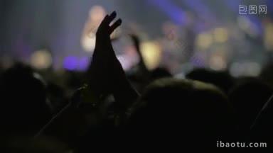 慢动作脱焦镜头的人兴奋与音乐会剪影鼓掌的手在前景和歌手在舞台上